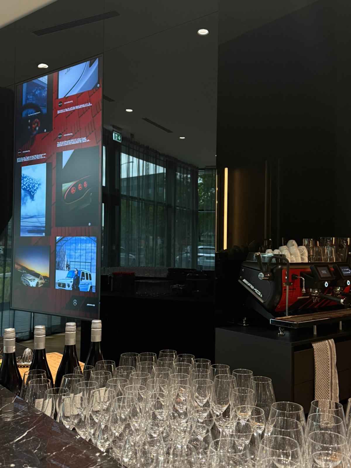 TIMELESS Event-Setup bei einem Mercedes-AMG Event: elegante Weingläser-Reihe an einer Marmorbar, dahinter Siebträger-Espressomaschine im AMG-Design und großformatiges Mercedes-AMG Display