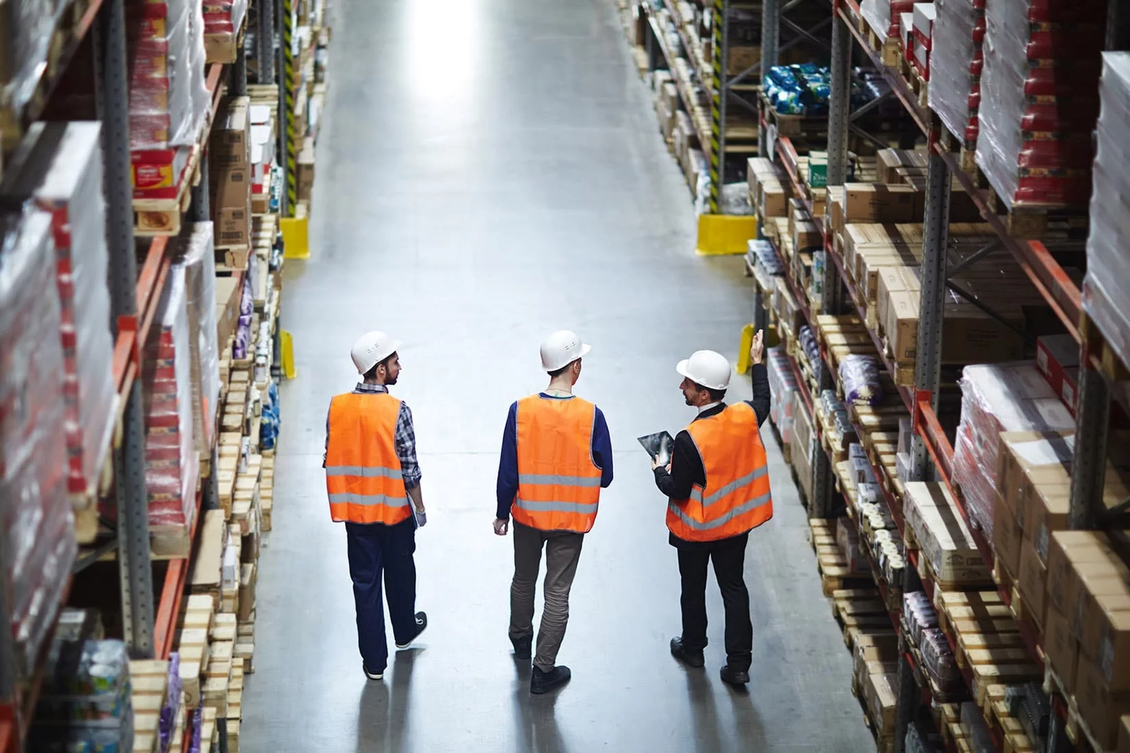 TIMELESS Lager- und Logistikpersonal mit Warnwesten und Schutzhelmen im Gang eines modernen Hochregallagers