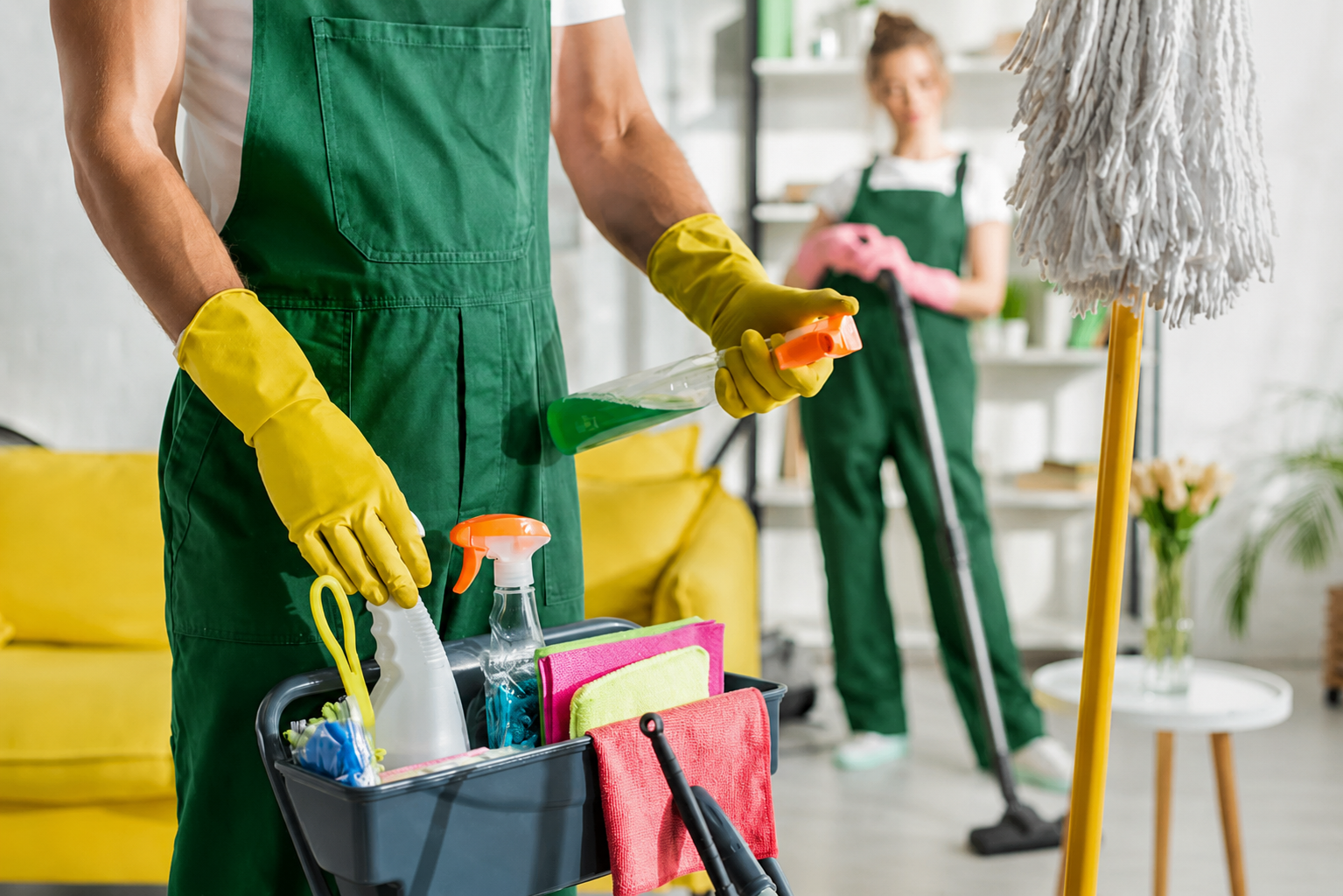 TIMELESS Reinigungskräfte in grüner Arbeitskleidung mit gelben Handschuhen bei der professionellen Unterhaltsreinigung eines hellen Wohnraums